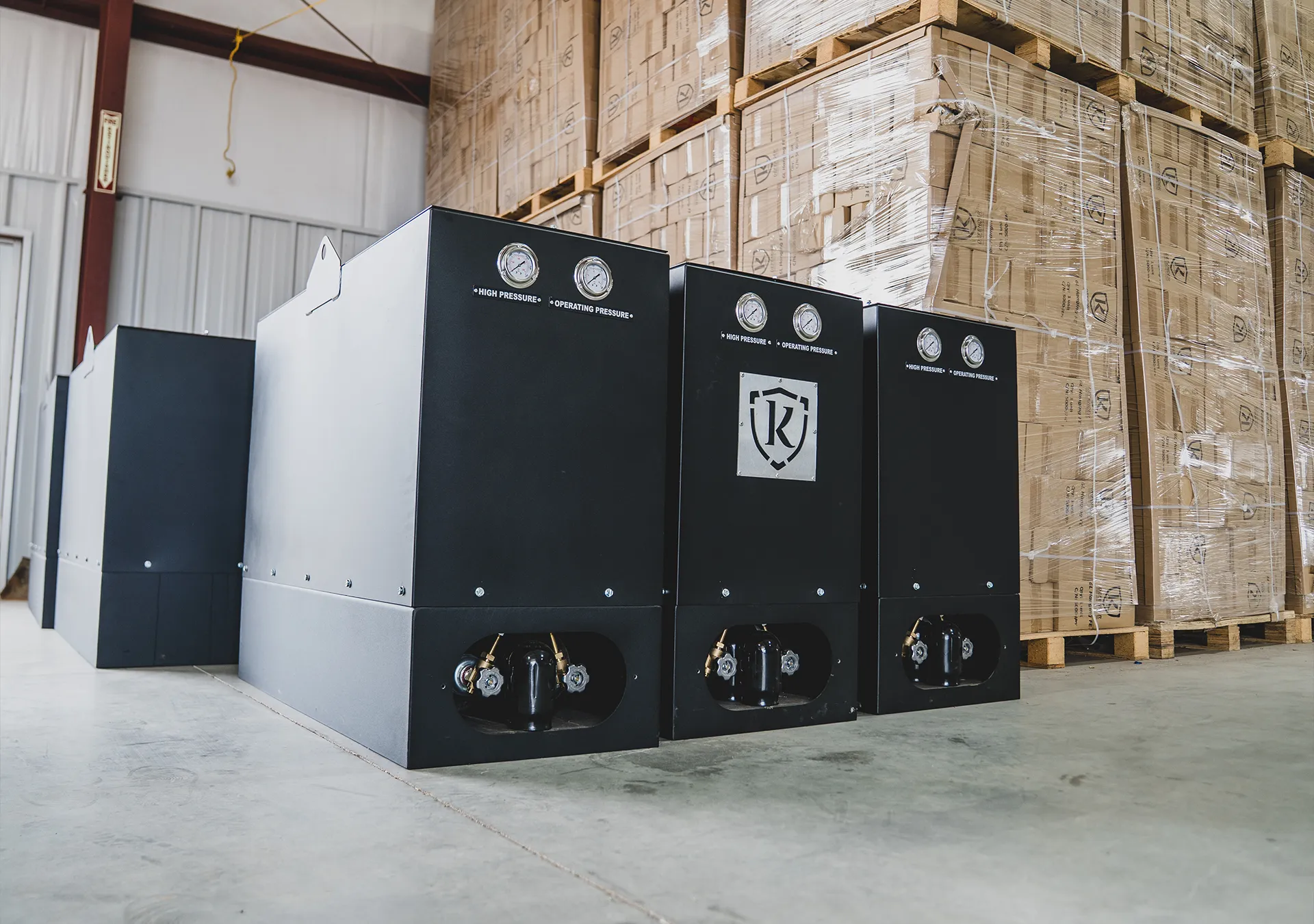 Row of black Knight Fire fire suppression system units with high pressure and operating pressure gauges, staged in a warehouse for shipment.