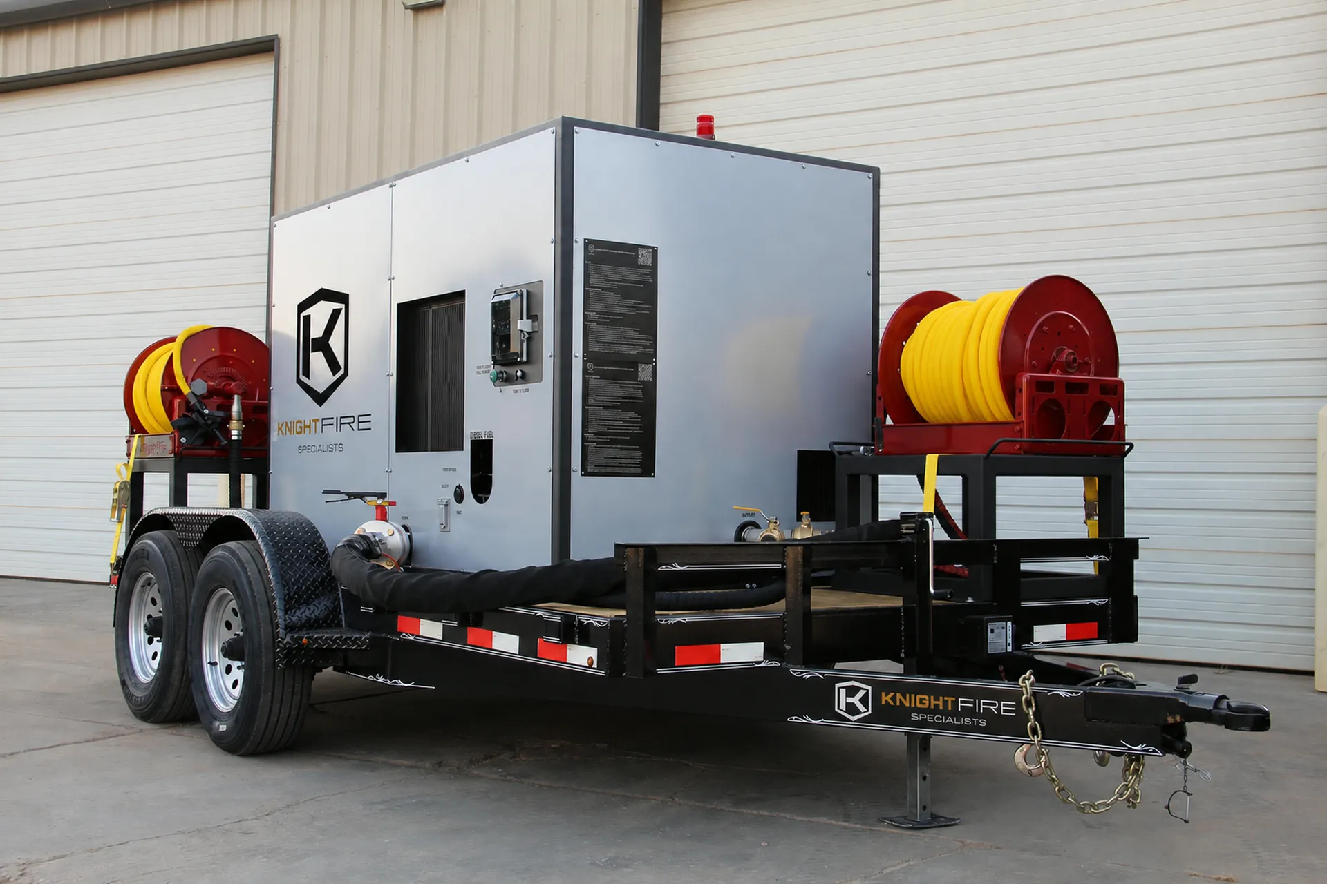 Trailer-mounted fire suppression equipment with yellow hoses coiled on red reels on each side.