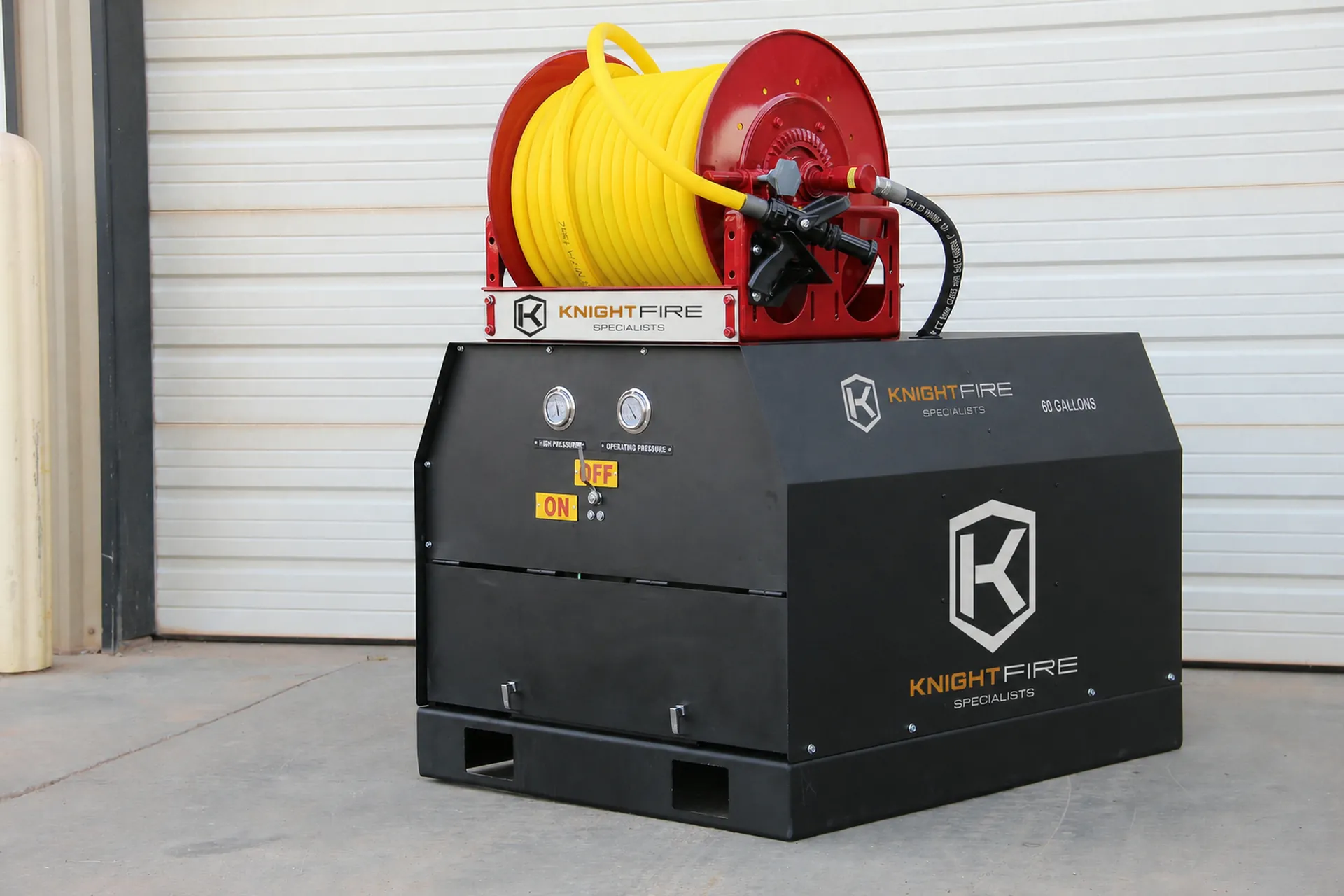 Black fire suppression system with yellow hose reel on concrete floor outside a closed garage door.